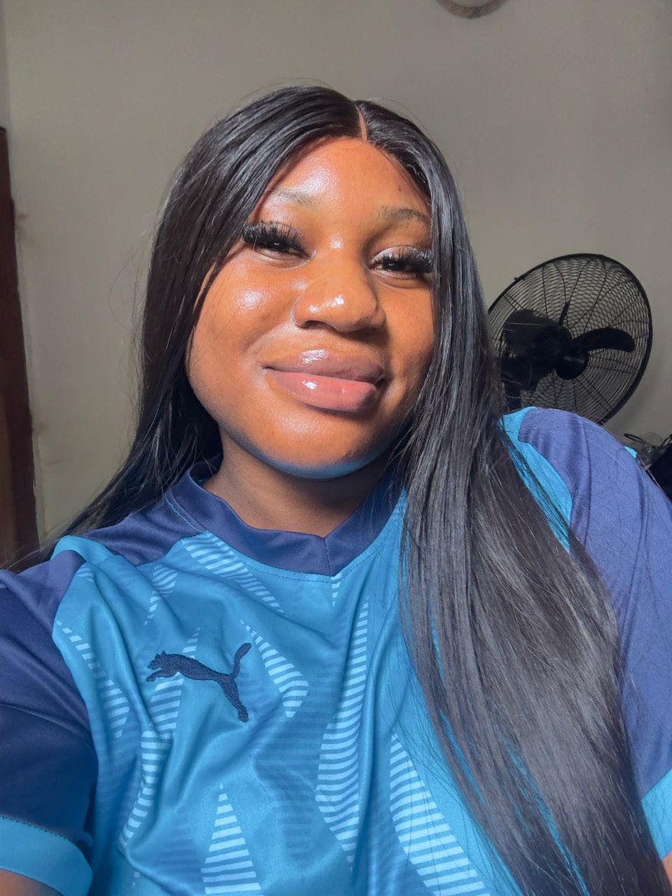 A woman in a blue sports shirt smiling into her phone