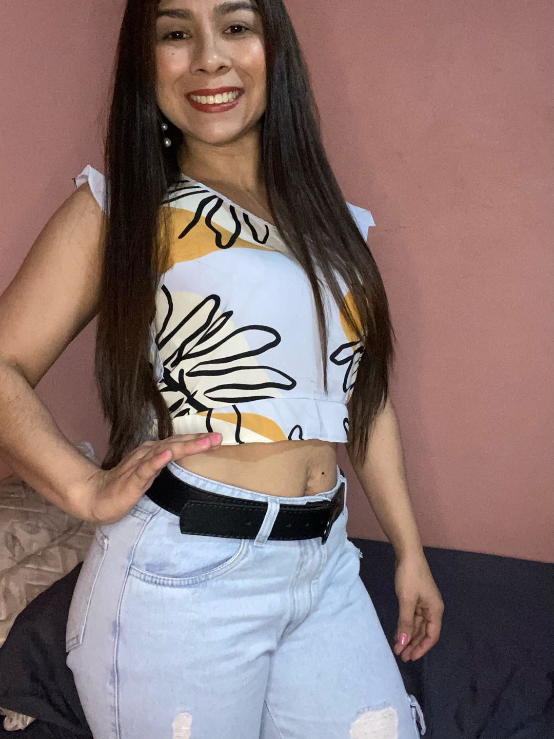 A smiling woman in a printed top standing in her room