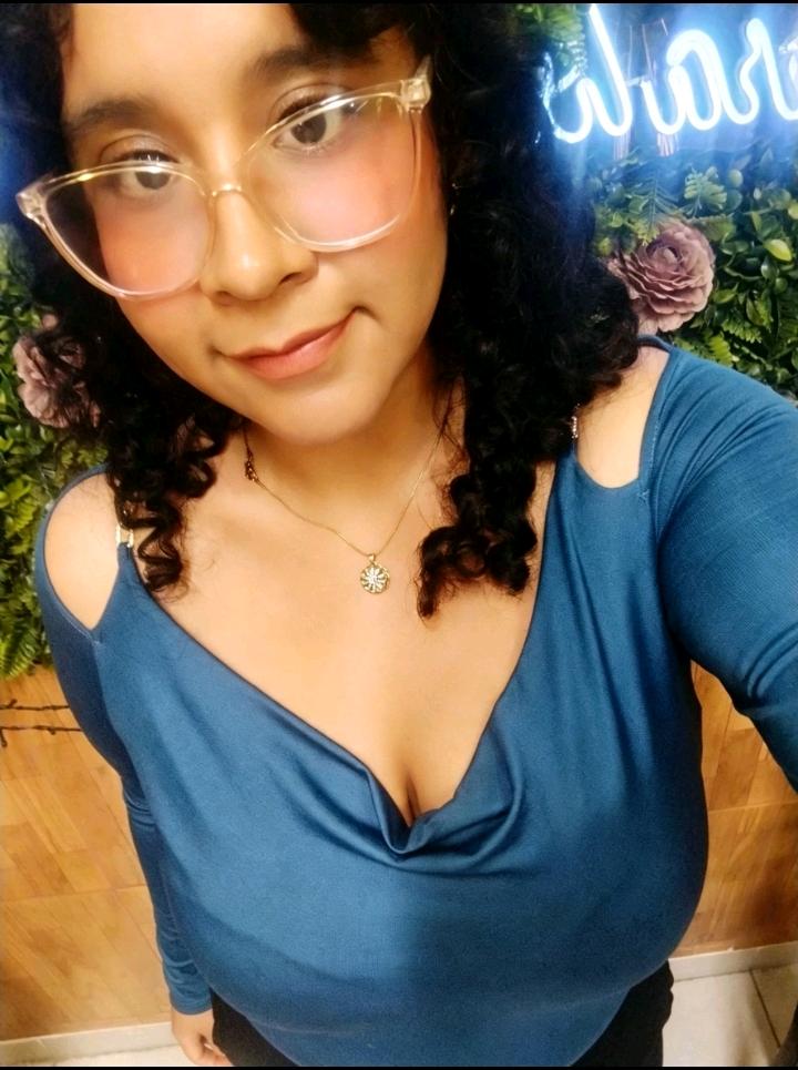 A woman with curly hair and glasses in a blue top